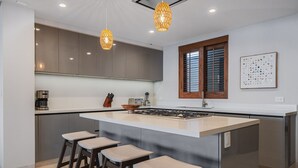 Een moderne keuken met een centraal eiland, barkrukken, hanglampen en een raam met jaloezieën.