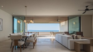 Een ruime woonkamer met een grote eettafel, comfortabele zitplaatsen en uitzicht op de oceaan.