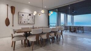 Een moderne eethoek met een grote tafel en stoelen, een hanglamp en uitzicht op zee.