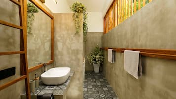A modern bathroom with a freestanding bathtub, a wooden-framed mirror, and a potted plant.