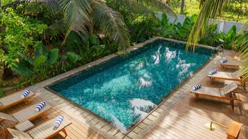A rectangular swimming pool with clear blue water, surrounded by lush greenery and wooden deck.