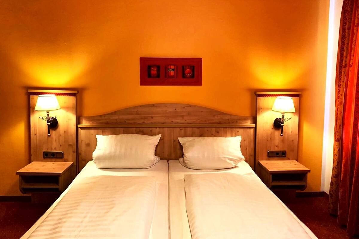 A double bed with two pillows, wooden headboard, two bedside tables with lamps, and a red-framed picture on the wall.
