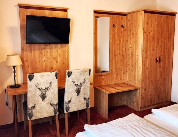 Een hotelkamer met een houten bureau, twee stoelen met hertenhoofdmotieven, een televisie, een kledingkast en een bed.
