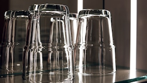 A row of clear glass tumblers on a reflective surface, likely a bar area. - Hotel Paintner (Germering)