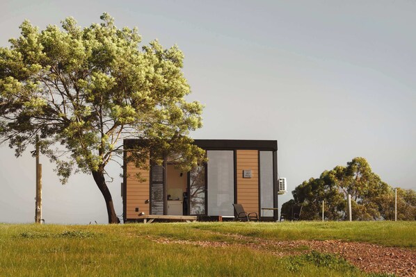 Un edificio moderno de una planta con techo plano, ventanas amplias y un área de estar exterior visible.