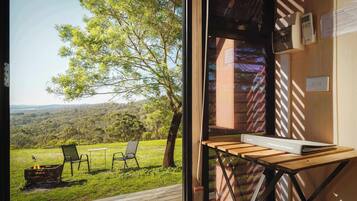 A room with a view of a grassy landscape and trees. There is a table with a book and a chair.