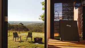 A room with a large glass door, a wooden table, two chairs, and a view of a hilly landscape.