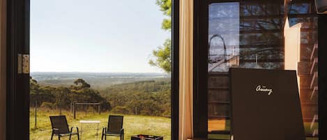 A room with a large glass door, a wooden table, two chairs, and a view of a hilly landscape.