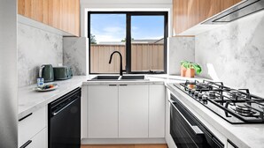 Eine moderne Küche mit weißen Schränken, einem schwarzen Wasserhahn, einem Fenster und einem Gasherd.
