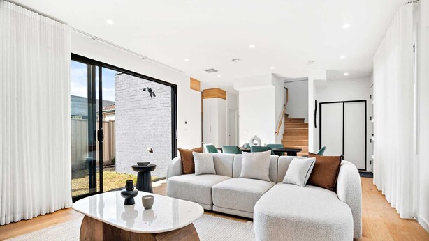Ein modernes Wohnzimmer mit einer großen Eckcouch, einem runden Couchtisch und einem Essbereich mit grünen Stühlen.