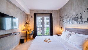 A modern hotel room with a large bed, a desk with a chair, a television, and a balcony with a city view. - The All New Stark Boutique Hotel (Kuta)