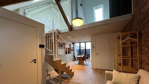 Un interno moderno con una scala, una zona pranzo e un angolo salotto con un divano.