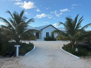 A modern villa with a gravel driveway, palm trees, and a sign reading "BLUE WATER VILLA". - Turtle Cove Villa - Walk to Beach, Restaurants, Smiths Reef and Snorkel. (Providenciales)