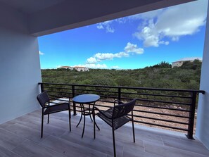A balcony with two chairs and a table, overlooking a hillside with buildings. - Turtle Cove Villa - Walk to Beach, Restaurants, Smiths Reef and Snorkel. (Providenciales)