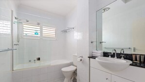 Un baño con ducha de vidrio, un inodoro, un lavabo con espejo y un perchero para toallas.