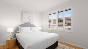 Un dormitorio con cama, dos lámparas de noche, una obra de arte enmarcada y una ventana con persianas.