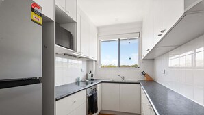 Cocina compacta con armarios blancos, encimera negra, una ventana y un distintivo de eficiencia energética visible.