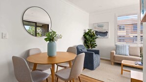 Una sala de estar moderna con una mesa redonda de madera, sillas tapizadas en gris, un sofá azul, un espejo grande y una planta en maceta.