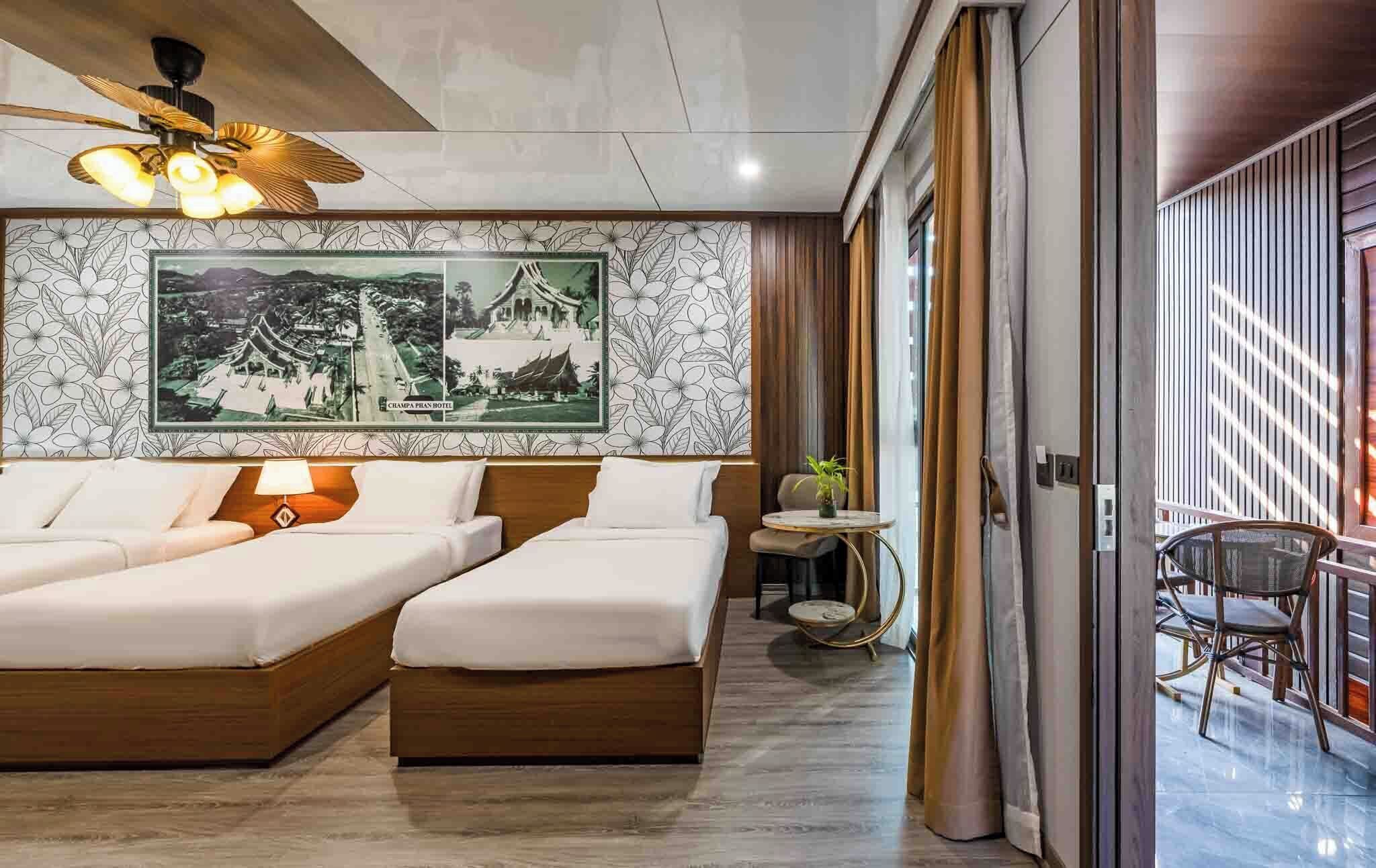 A hotel room with two beds, a ceiling fan, a wall with a floral pattern, and a view of the outside.