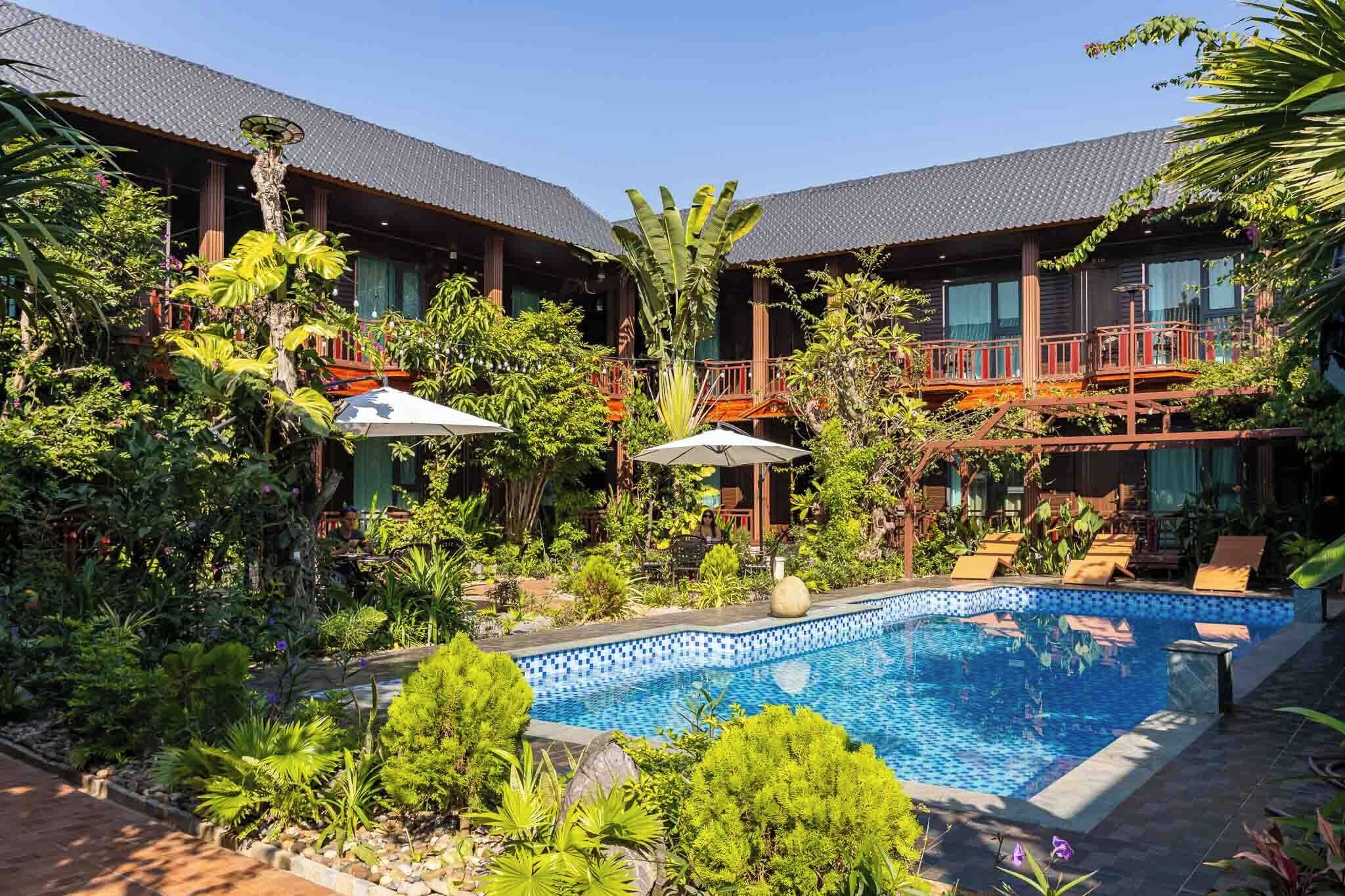 Piscina rodeada por vegetação exuberante e um edifício com telhado em azulejos.