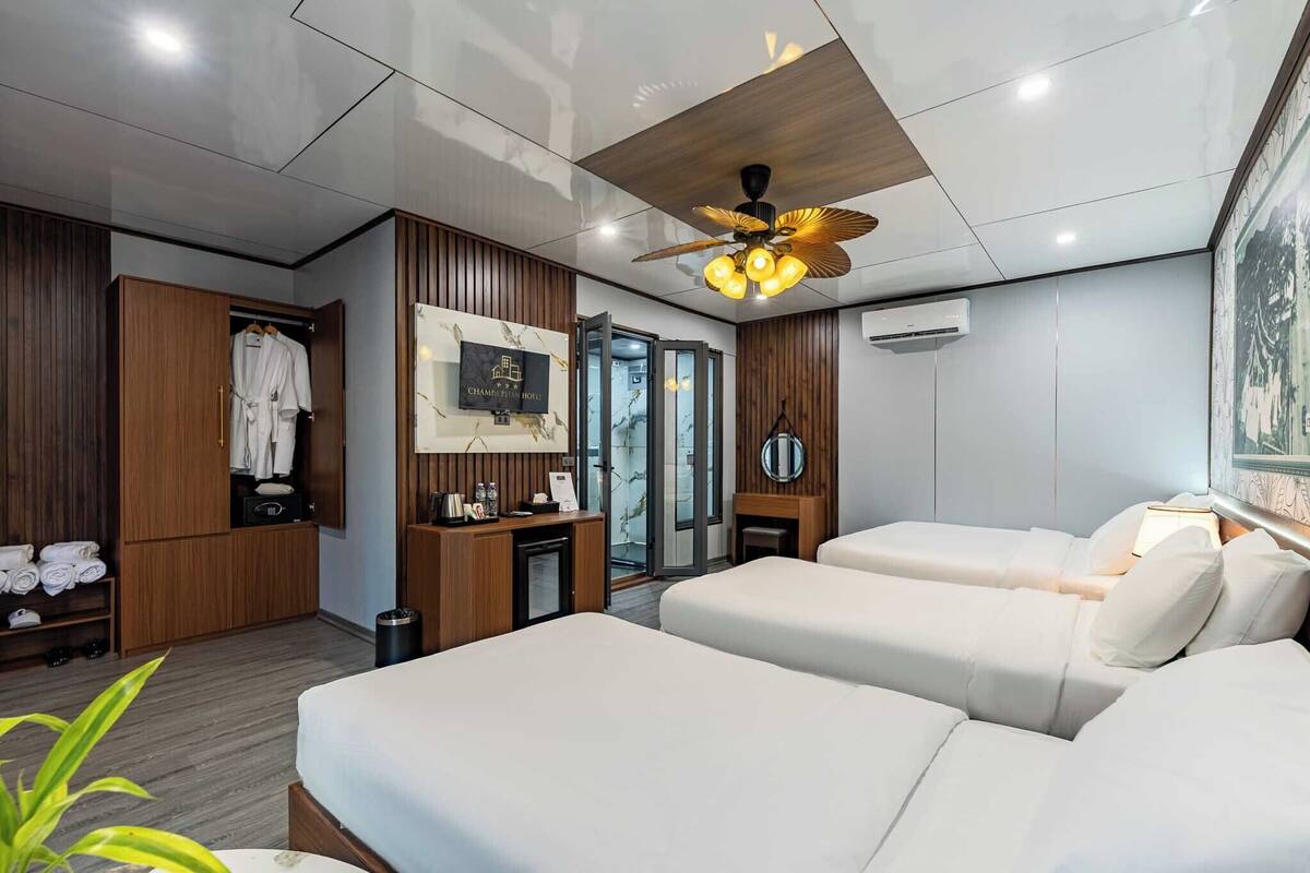 Habitación de hotel con dos camas, un armario, un escritorio, un ventilador de techo y un cuadro en la pared.