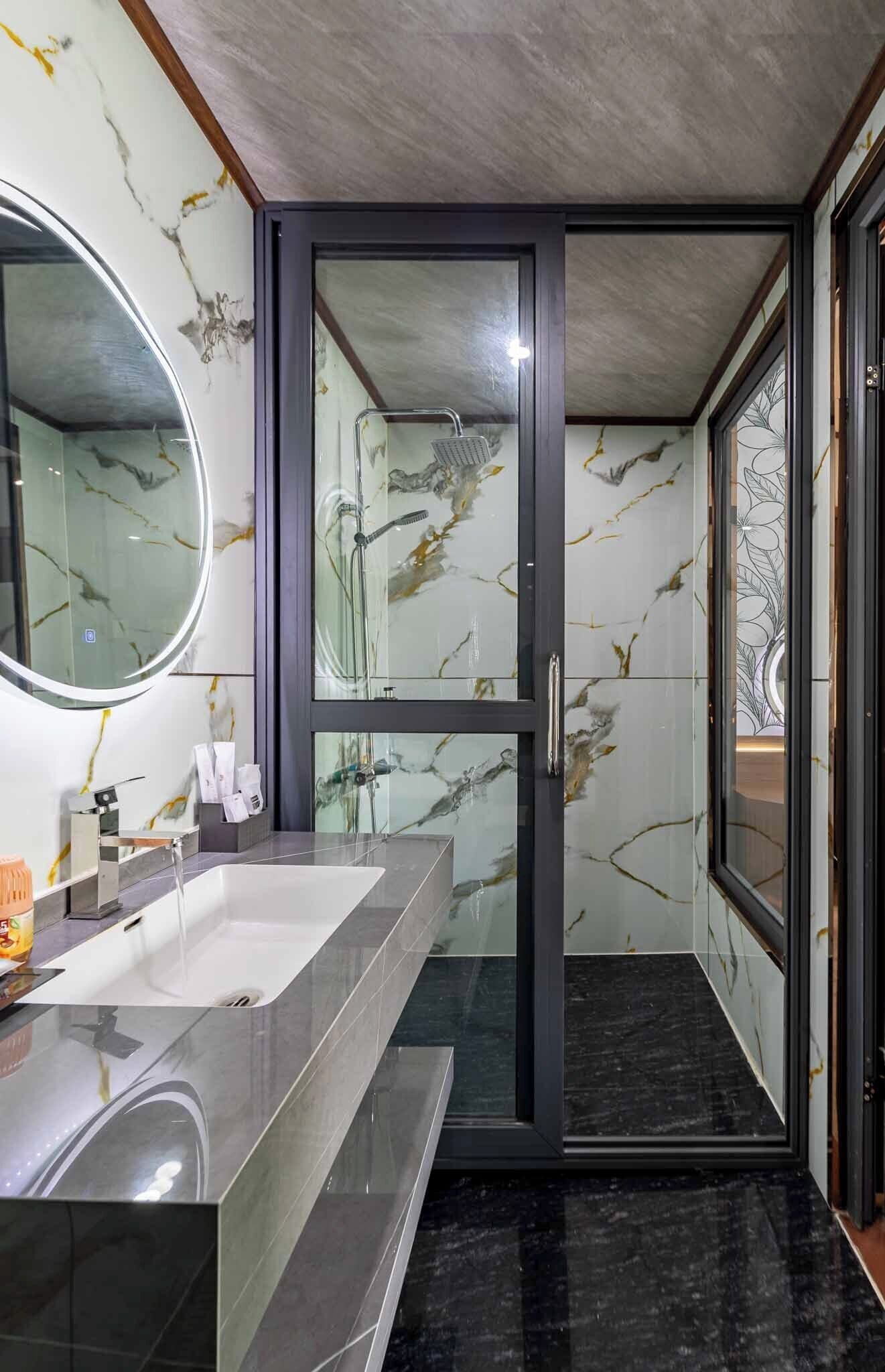 A modern bathroom with a glass shower enclosure, a large mirror, and a marble-tiled wall.