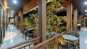 A spacious indoor area with multiple seating arrangements, wooden columns, and a central plant display. - Champa Phan Boutique Hotel (Vientiane)