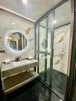 A modern bathroom with a glass shower enclosure, a marble backsplash, and a round mirror with built-in lighting.