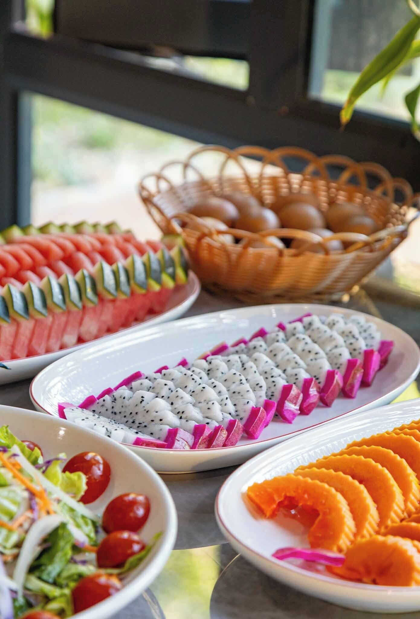 Una mesa con diversos alimentos, entre ellos sandía, pitahaya y una ensalada.