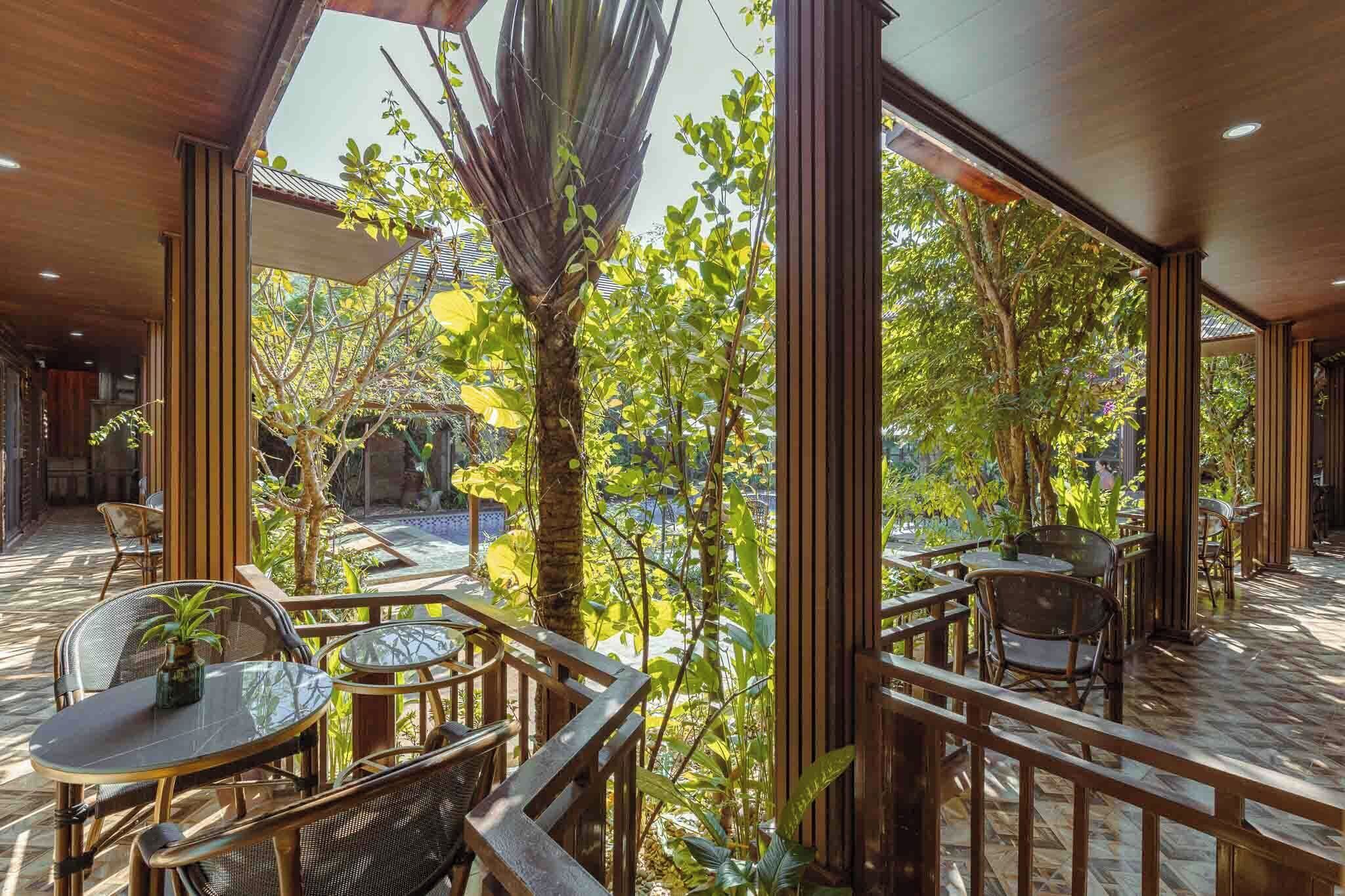 An outdoor seating area with tables and chairs, surrounded by wooden railings and lush greenery.