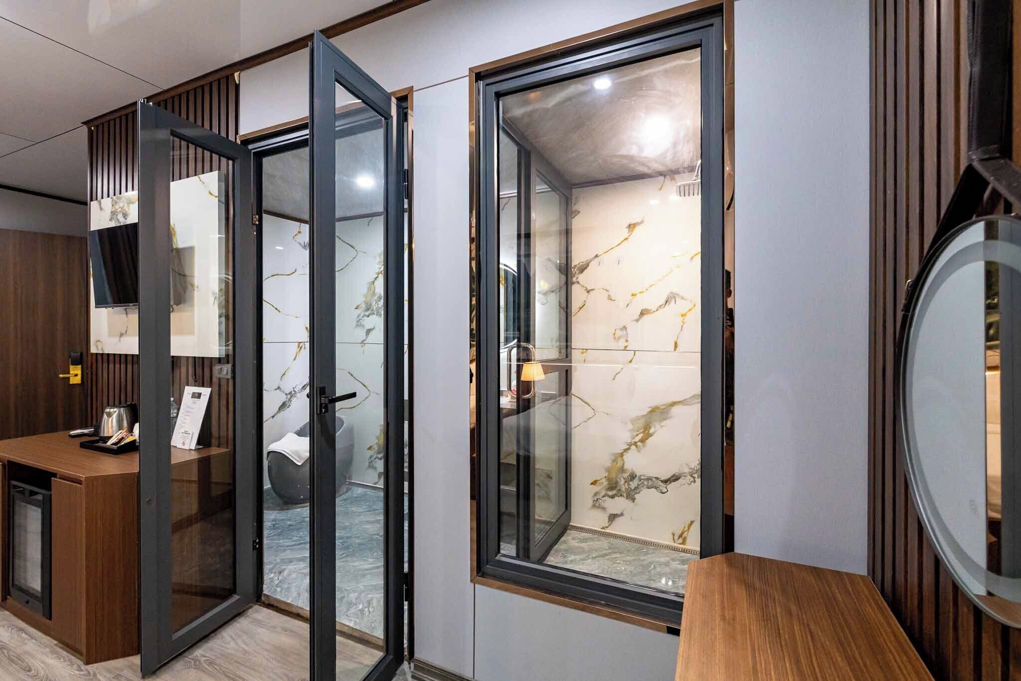 Una habitación de hotel moderna con un escritorio de madera, un vidrio que da al baño y una pared de mármol.