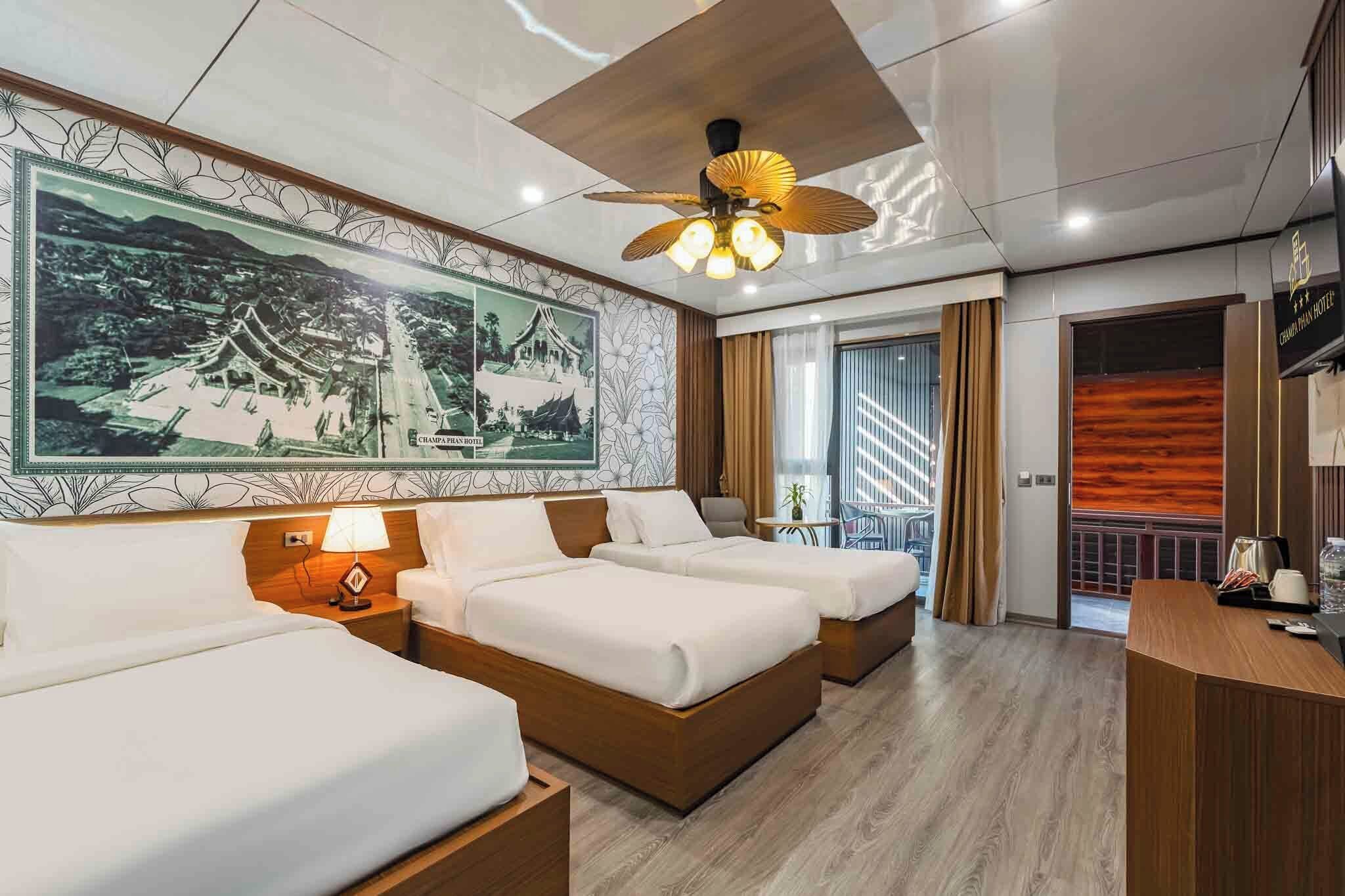 Habitación de hotel con dos camas, ventilador de techo, un mural grande en la pared, un escritorio y vistas al exterior.