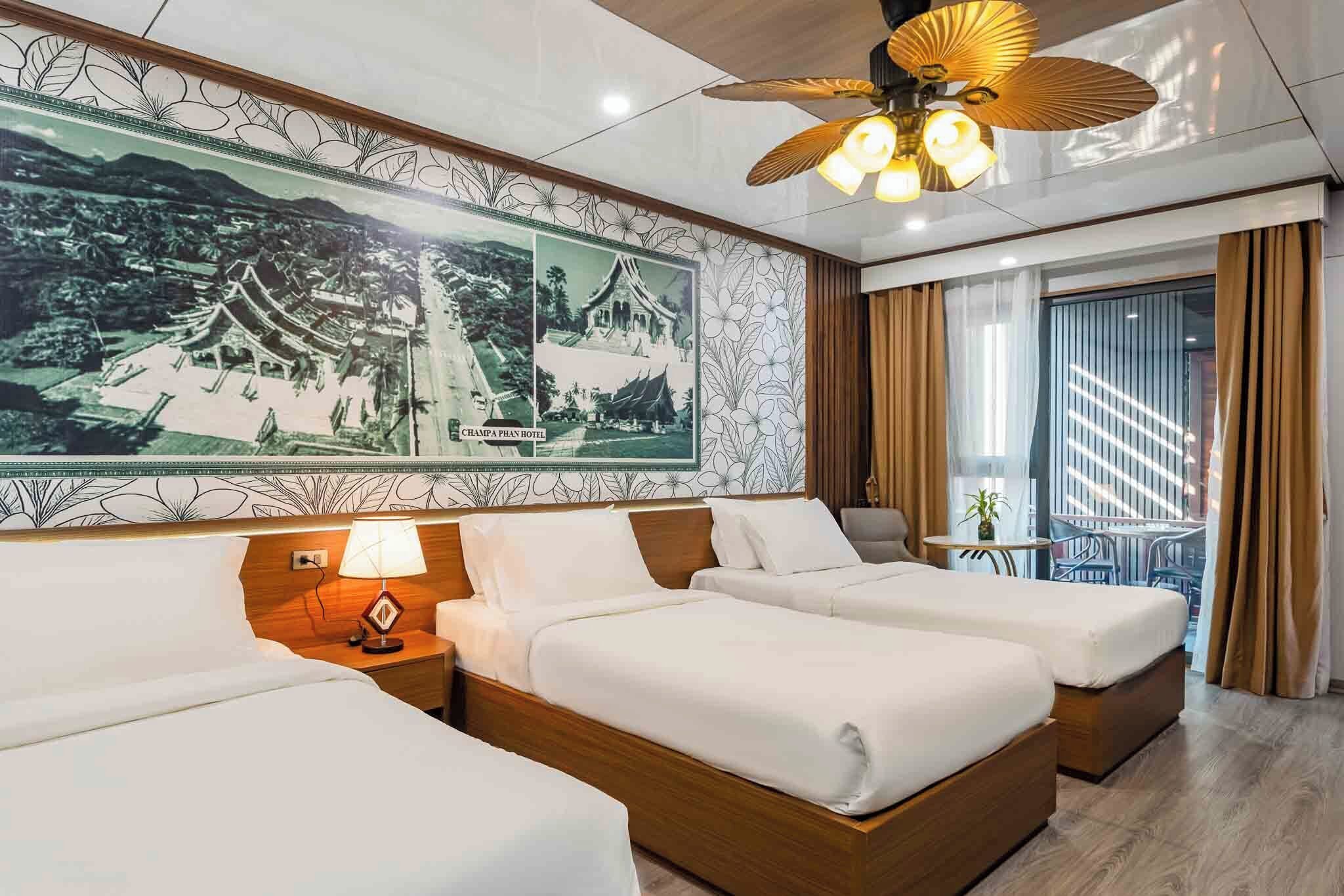 A hotel room with two beds, a ceiling fan, a large poster of traditional architecture, and a view of a balcony.