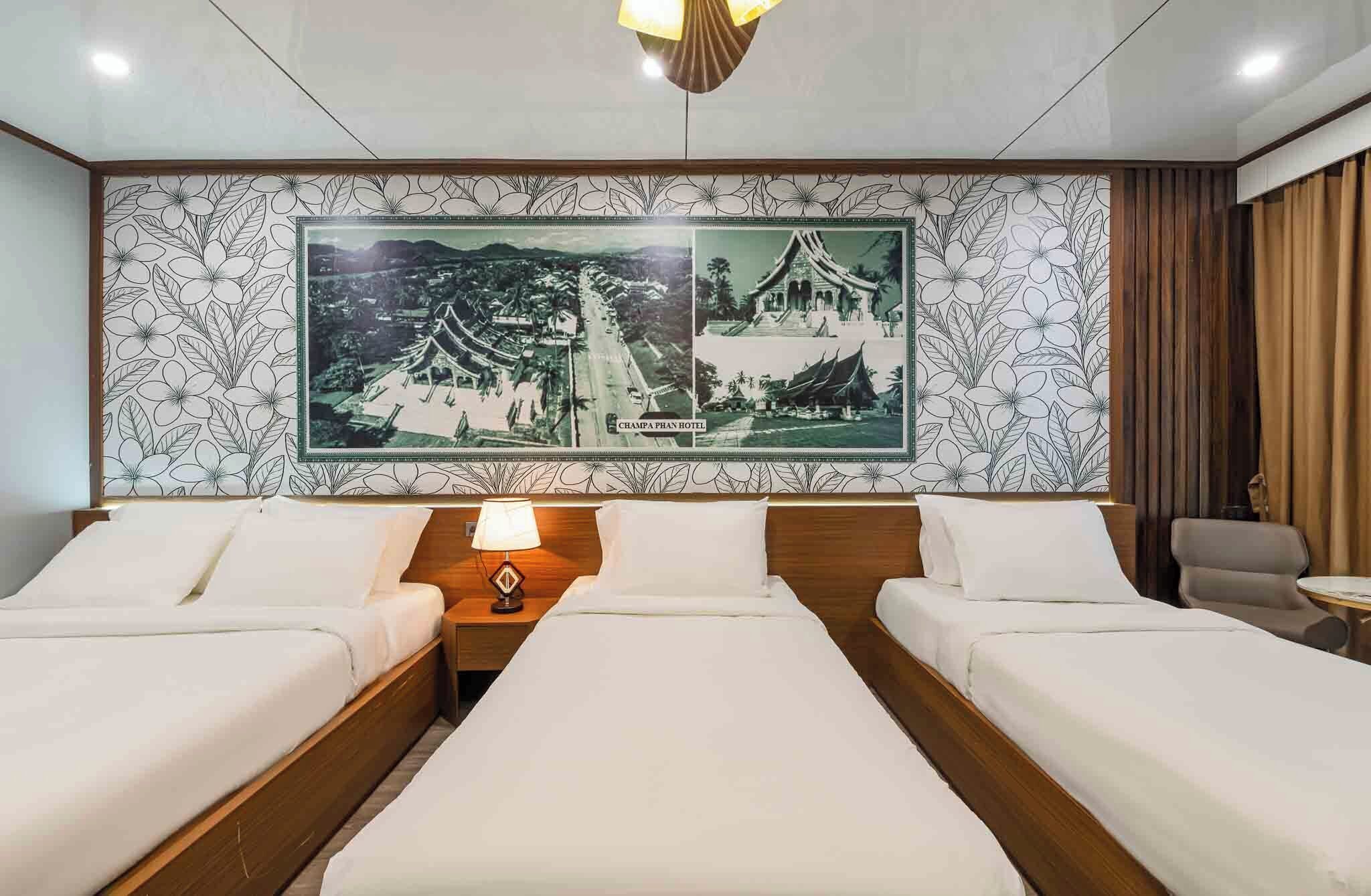 Habitación de hotel con dos camas, una mesita de noche con lámpara, un cuadro grande con un edificio tradicional y vista al interior de la habitación.
