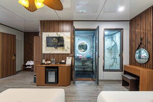 A hotel reception area with a wooden reception desk, a mounted TV, and a glass door leading to a room.