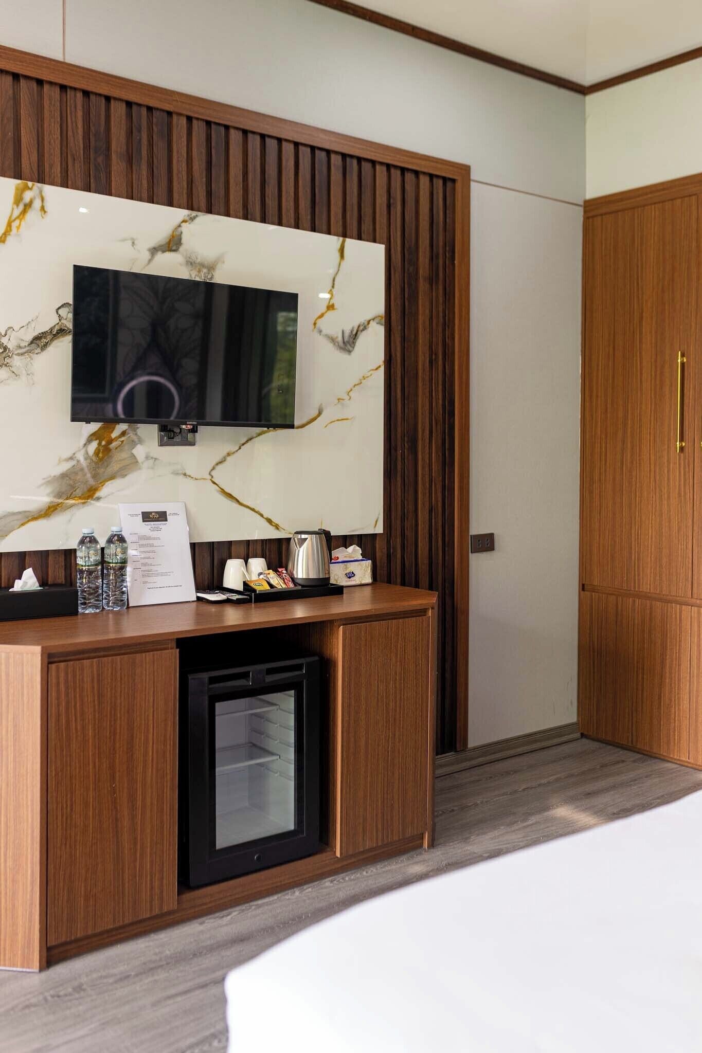 Een hotelkamer met een houten bureau, een flatscreen televisie bevestigd aan een marmeren muur, een minibar en een kledingkast.