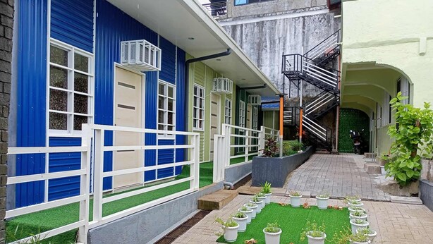 Une cour avec un bâtiment bleu, une clôture blanche et une pelouse verdoyante agrémentée de plantes en pot.