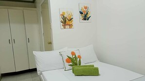 Une chambre à coucher avec un lit, des murs blancs et deux tableaux représentant des motifs floraux, encadrés.
