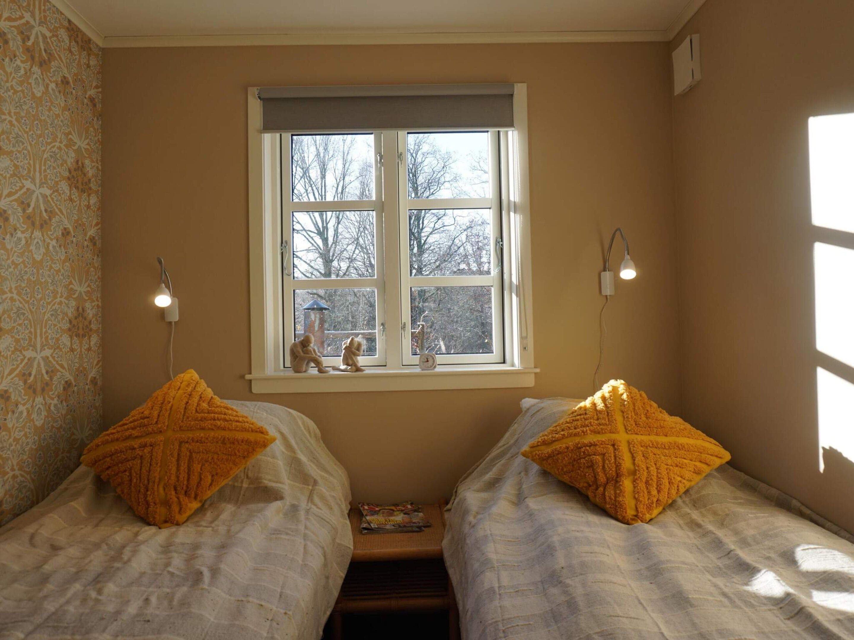 Une chambre avec deux lits, une fenêtre et une lampe fixée au mur.