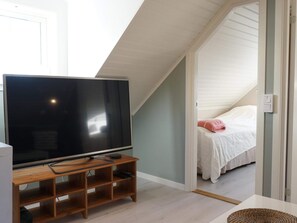 Ett rum med en tv-apparat på ett träställ, en säng med vita sängkläder och ett sluttande tak.