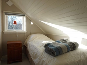 A bedroom with a sloped ceiling, a single bed with a blanket, a nightstand, a lamp, and a window with a view of trees. - 4 Person Holiday Home in Tanumshede (Tanum)