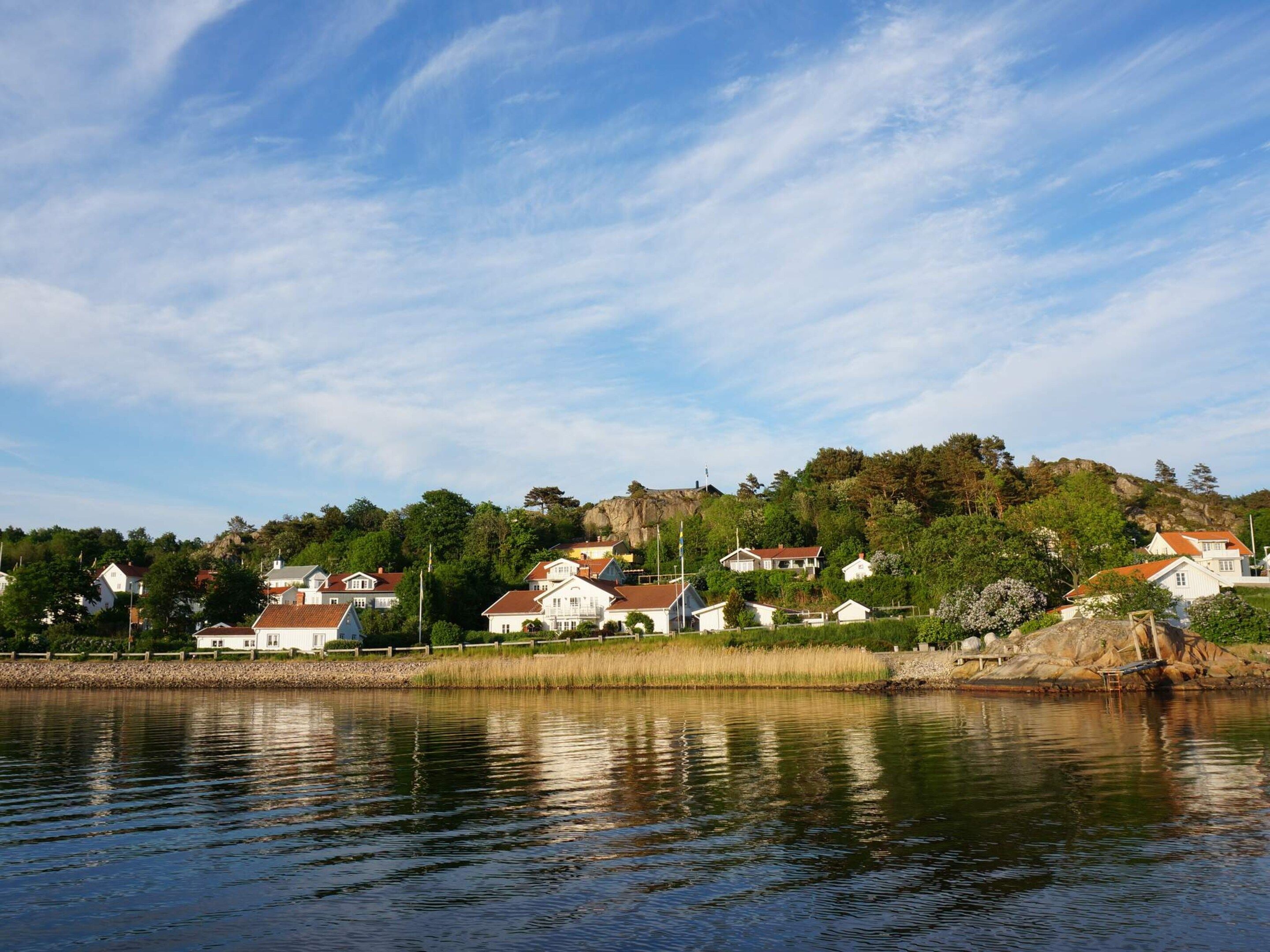 A lakeside residential area with houses, a rocky hill, and a clear sky.