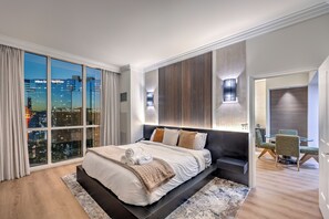 Ein modernes Hotelzimmer mit großem Bett, Blick auf die Stadt und einer Essecke mit Stühlen.