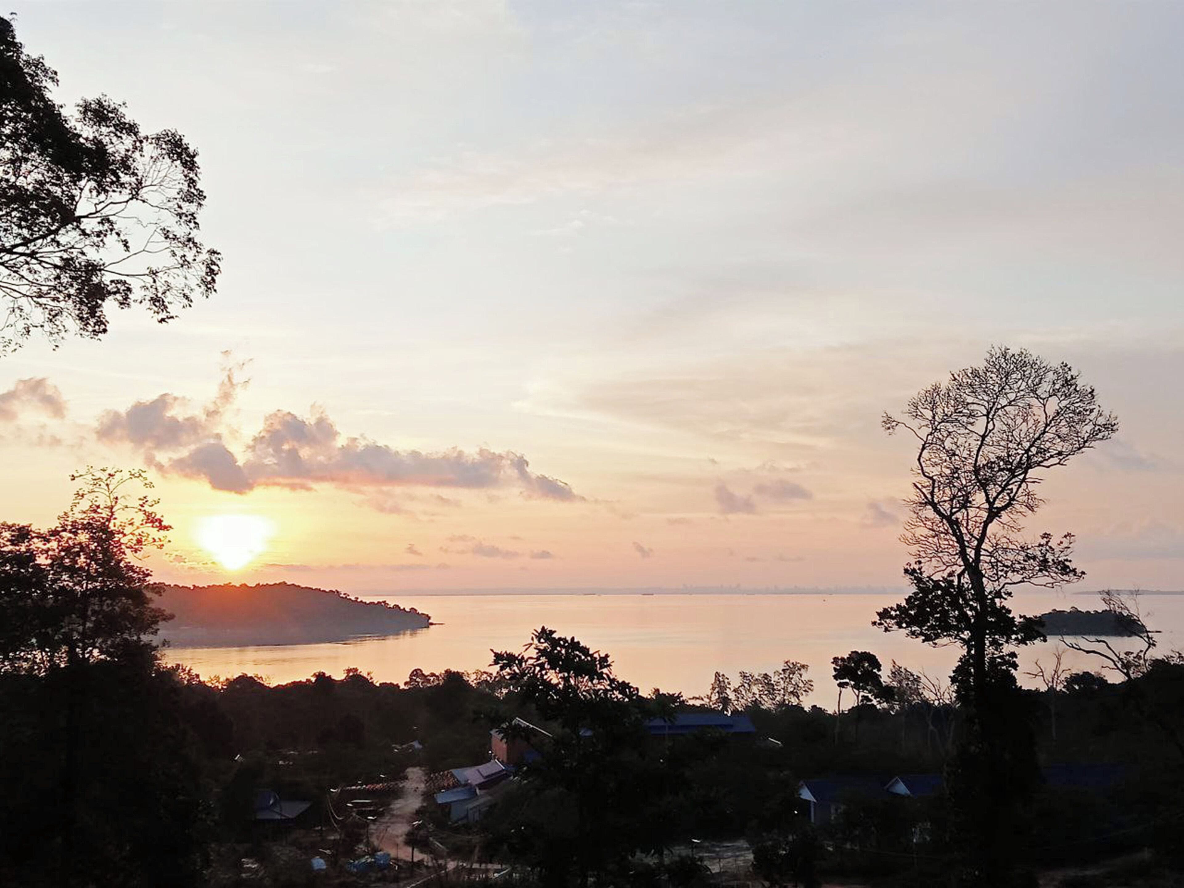 Un paisaje costero con un atardecer sobre el agua, rodeado de árboles y edificios.