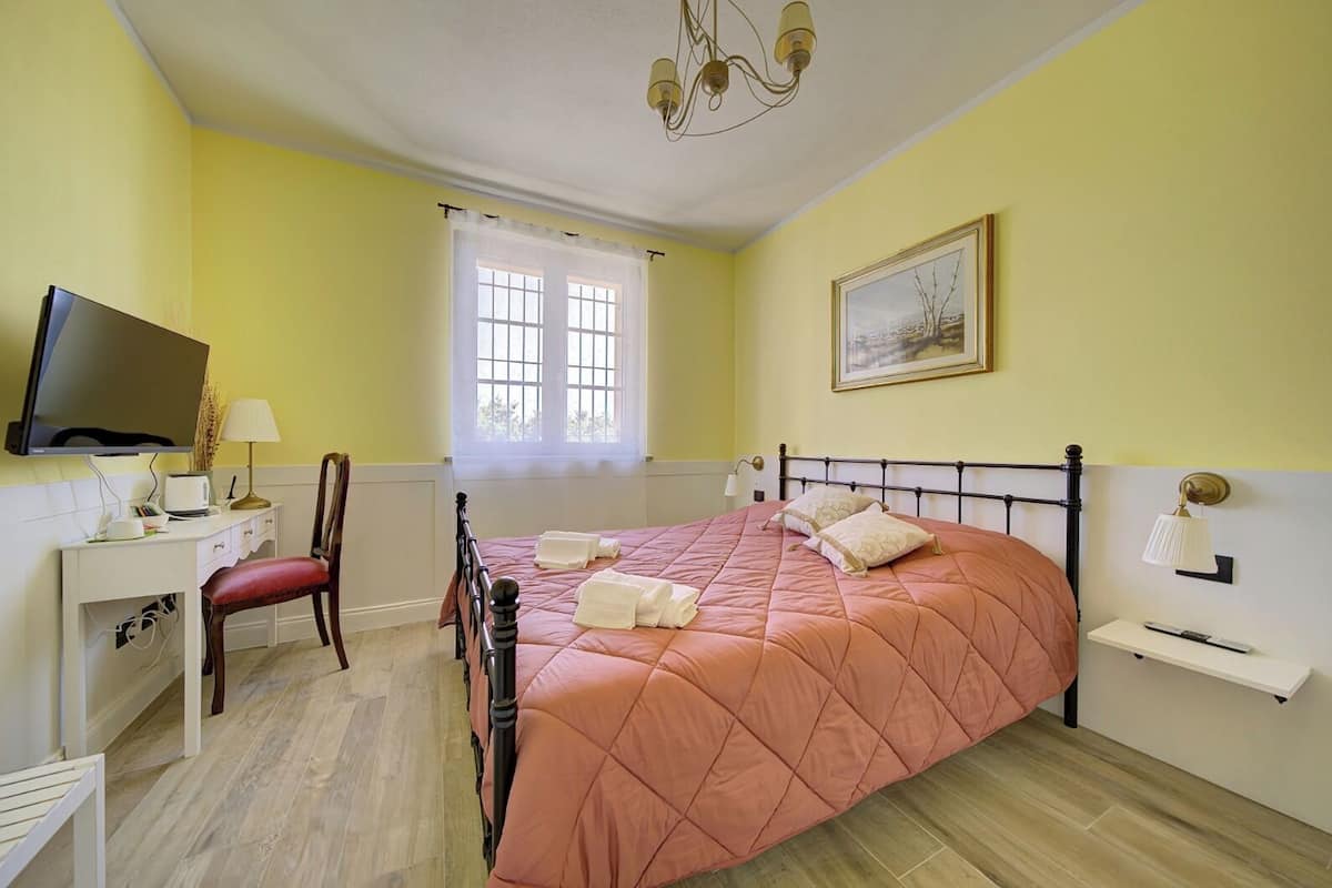 A bedroom with a bed, a desk, a chair, a television, and a window with curtains.