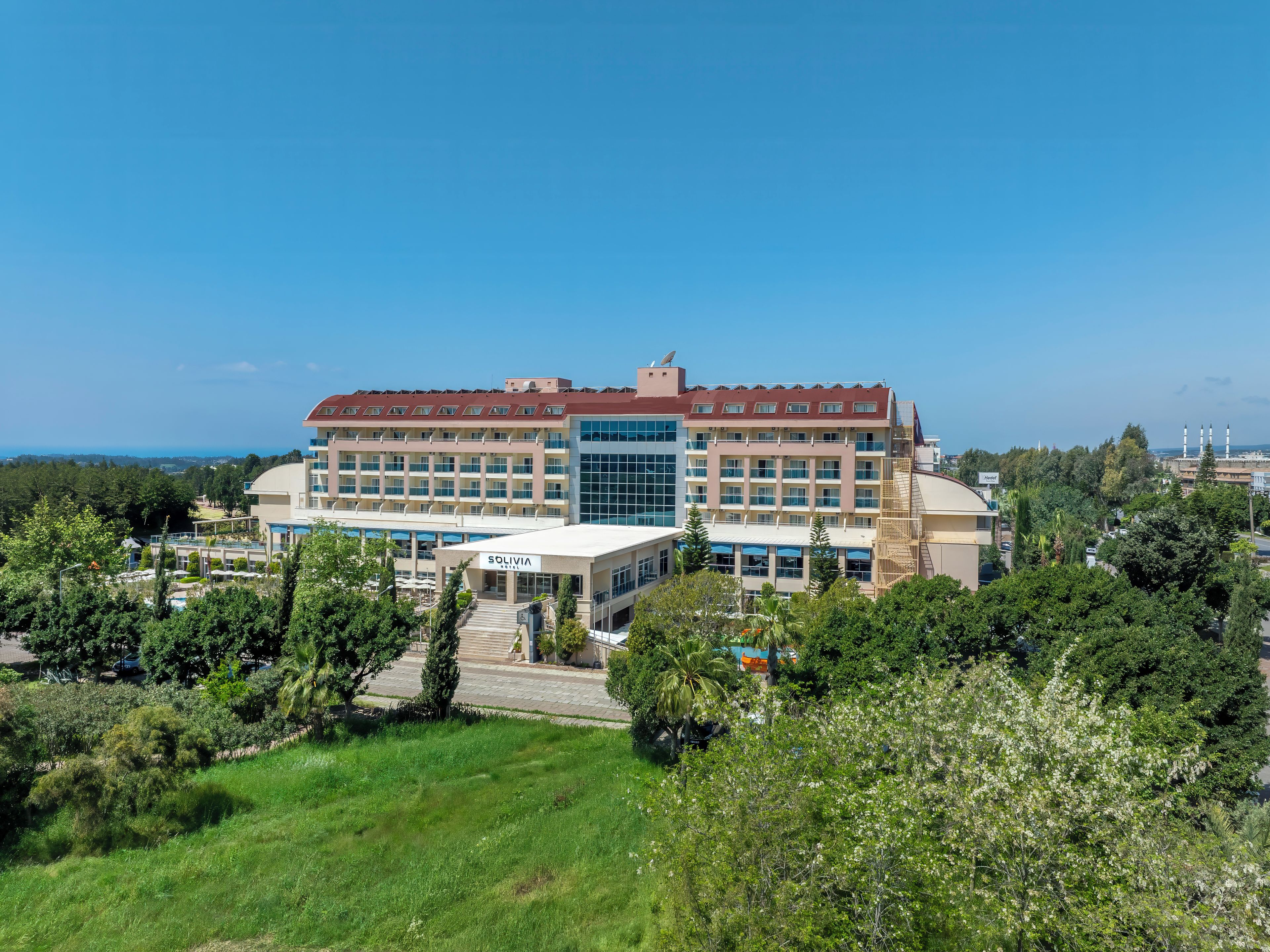 A multi-story hotel with a central atrium, surrounded by greenery and a clear sky.