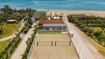 Una propiedad costera con cancha de tenis, un edificio con techo rojo y una playa al fondo.