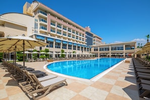 A hotel with a swimming pool, sun loungers, and umbrellas.