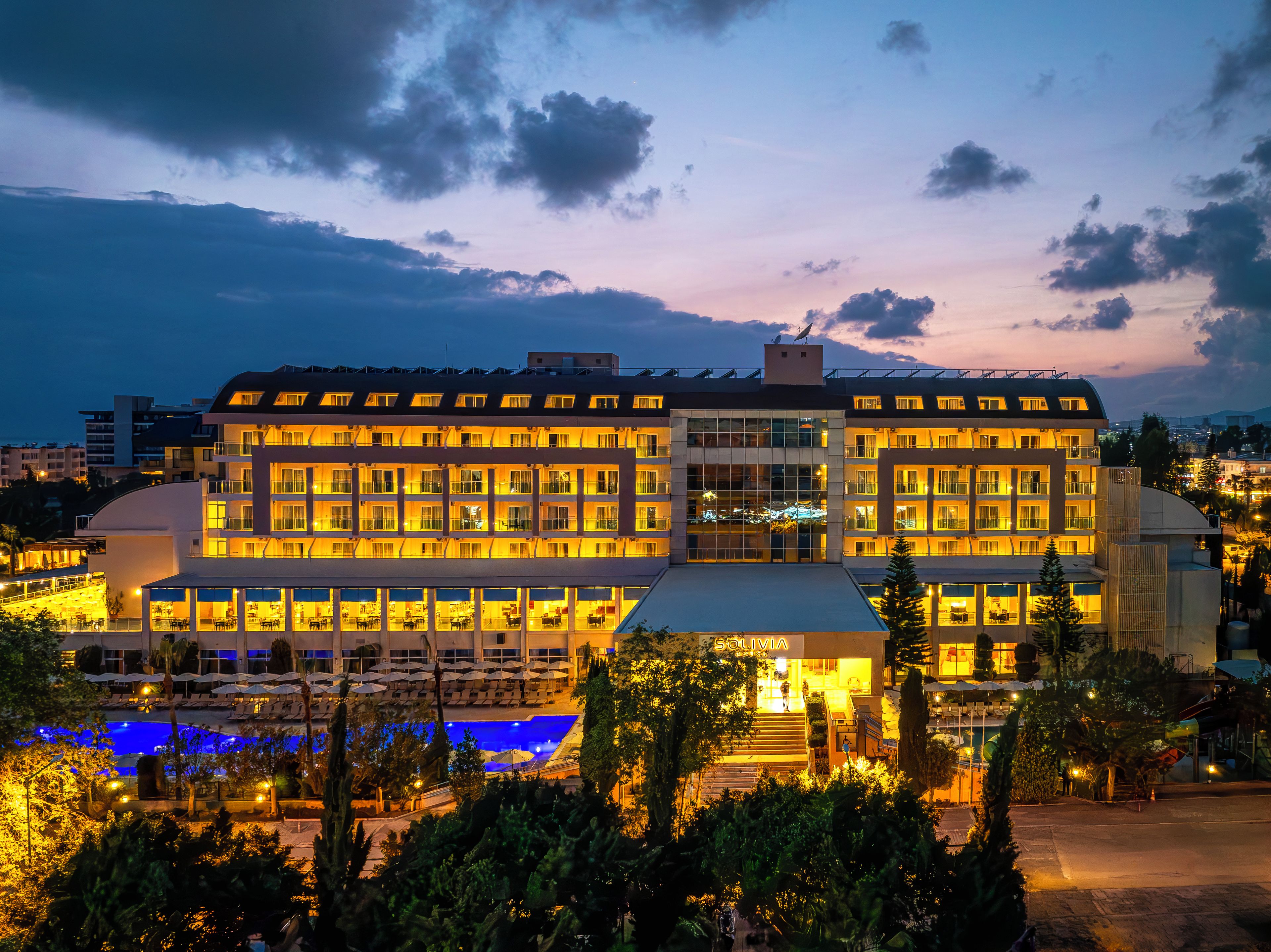 Un hotel con varios pisos, piscina y fachada bien iluminada.