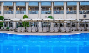 A swimming pool with lounge chairs and umbrellas, a building with multiple floors and large windows, and a clear sky. - Solivia Hotel (Konaklı)
